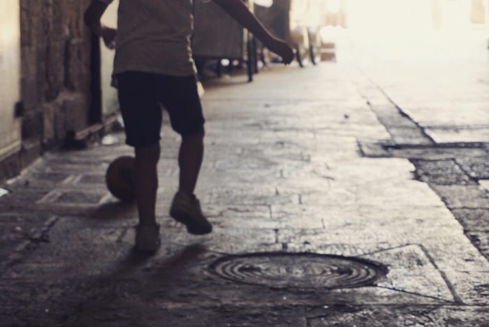 路地でサッカーする少年